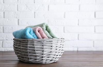 Photo of Wicker basket with soft bath towels on wooden table near white brick wall