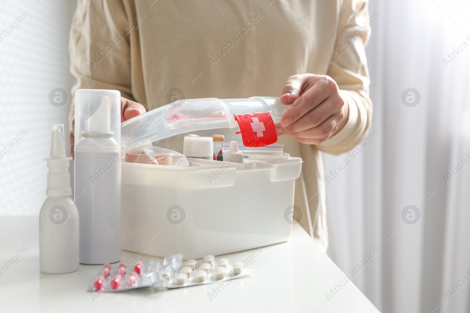 Photo of Woman opening first aid kit at white table indoors, closeup. Space for text