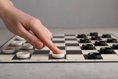 Woman moving checker on board at light grey table, closeup