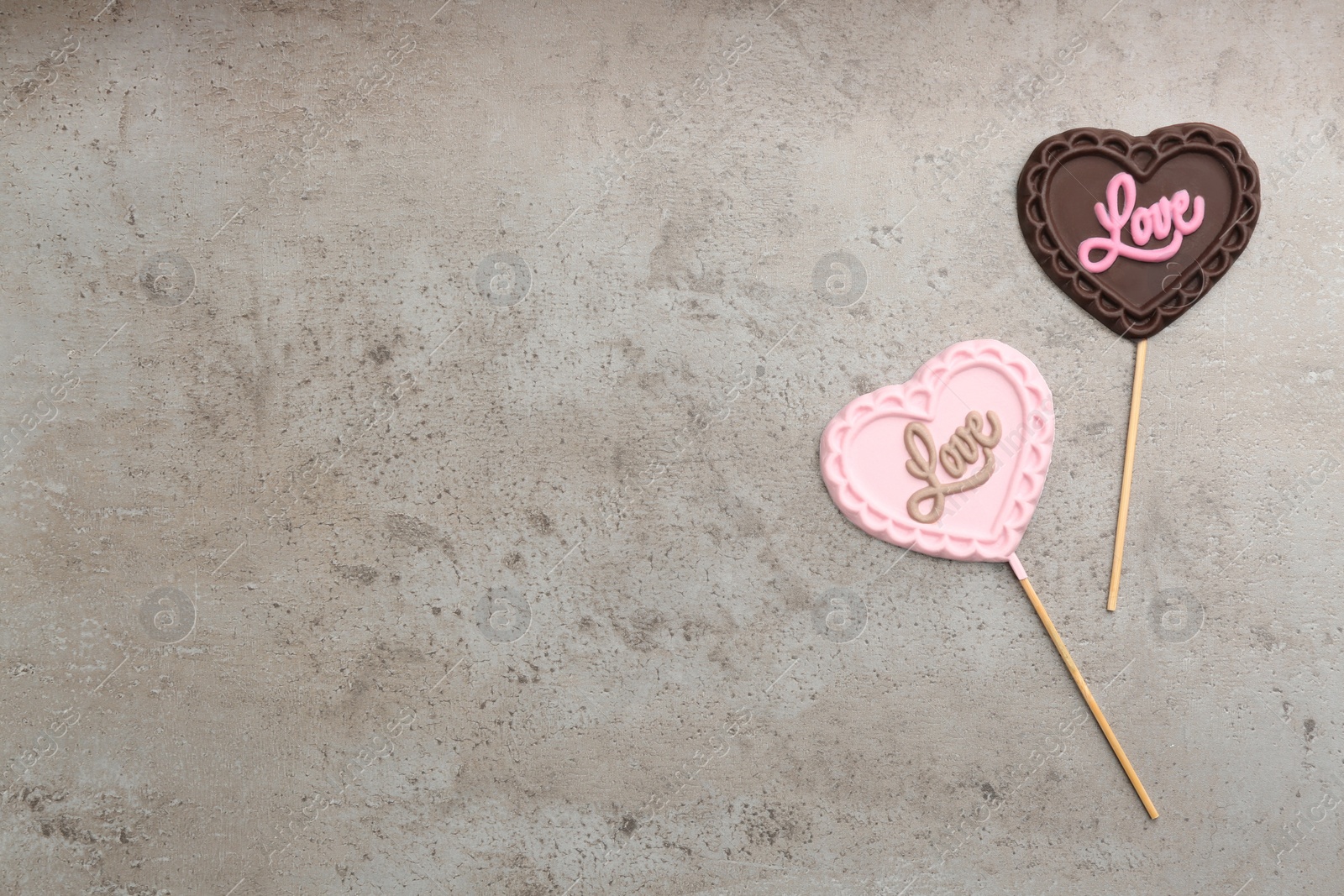 Photo of Different chocolate heart shaped lollipops with word Love on grey table, flat lay. Space for text