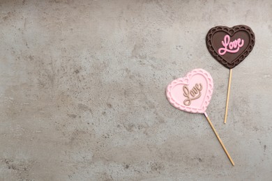 Different chocolate heart shaped lollipops with word Love on grey table, flat lay. Space for text