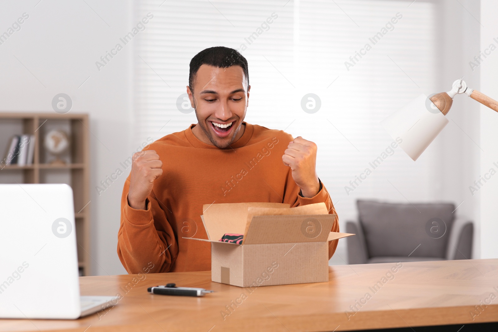 Photo of Emotional young man near parcel at wooden table. Internet shopping