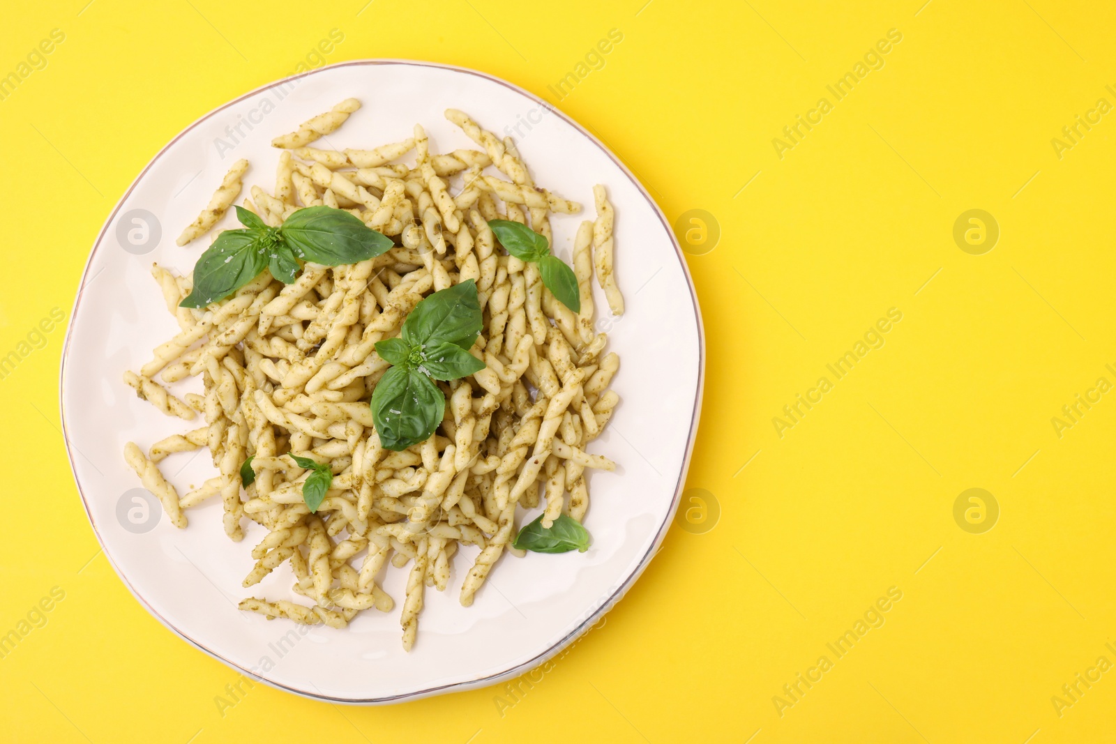 Photo of Plate of delicious trofie pasta with pesto sauce and basil leaves on yellow background, top view. Space for text
