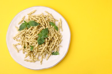 Plate of delicious trofie pasta with pesto sauce and basil leaves on yellow background, top view. Space for text