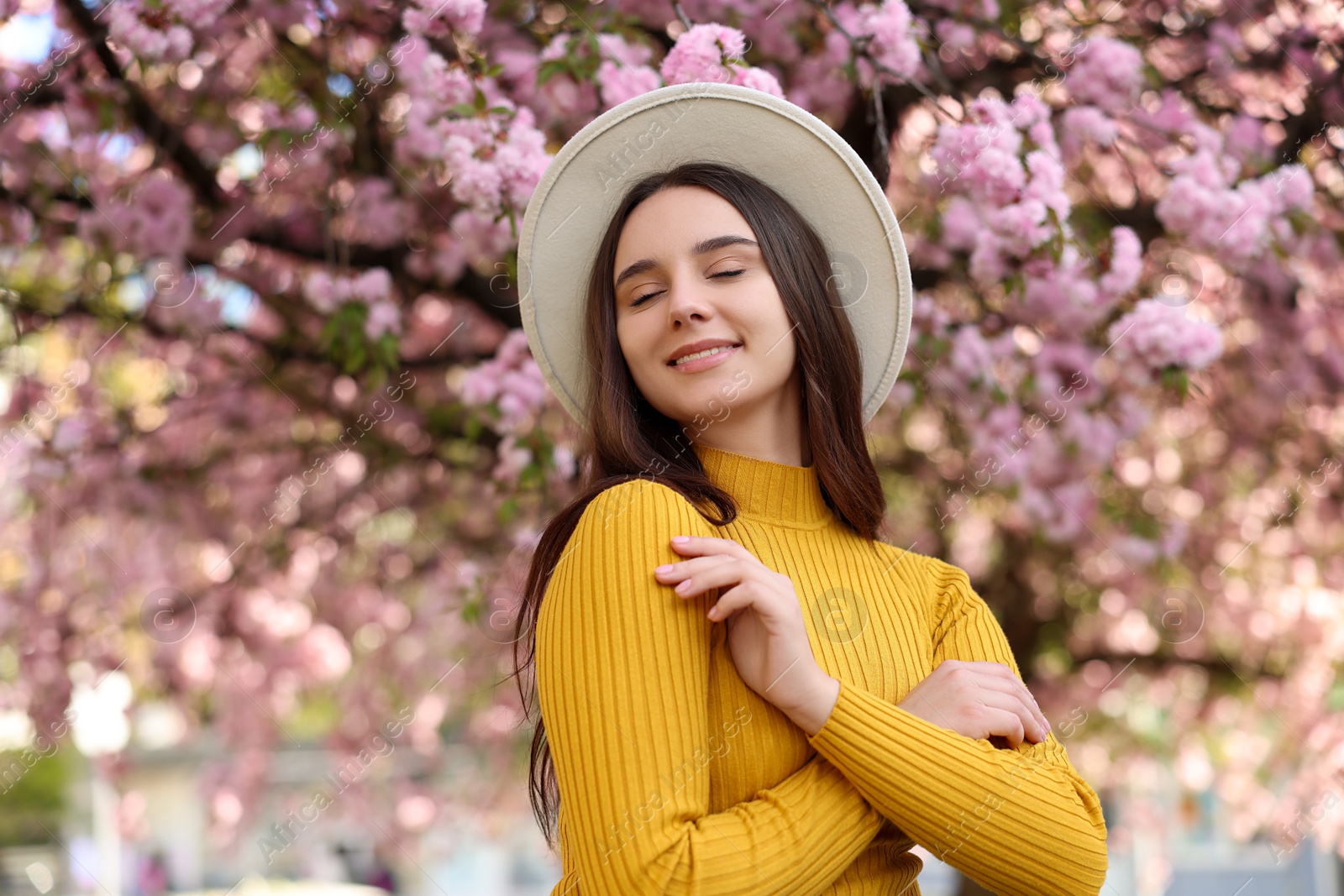 Photo of Beautiful woman in hat near blossoming tree on spring day, space for text