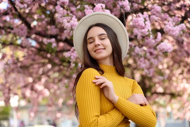 Beautiful woman in hat near blossoming tree on spring day, space for text