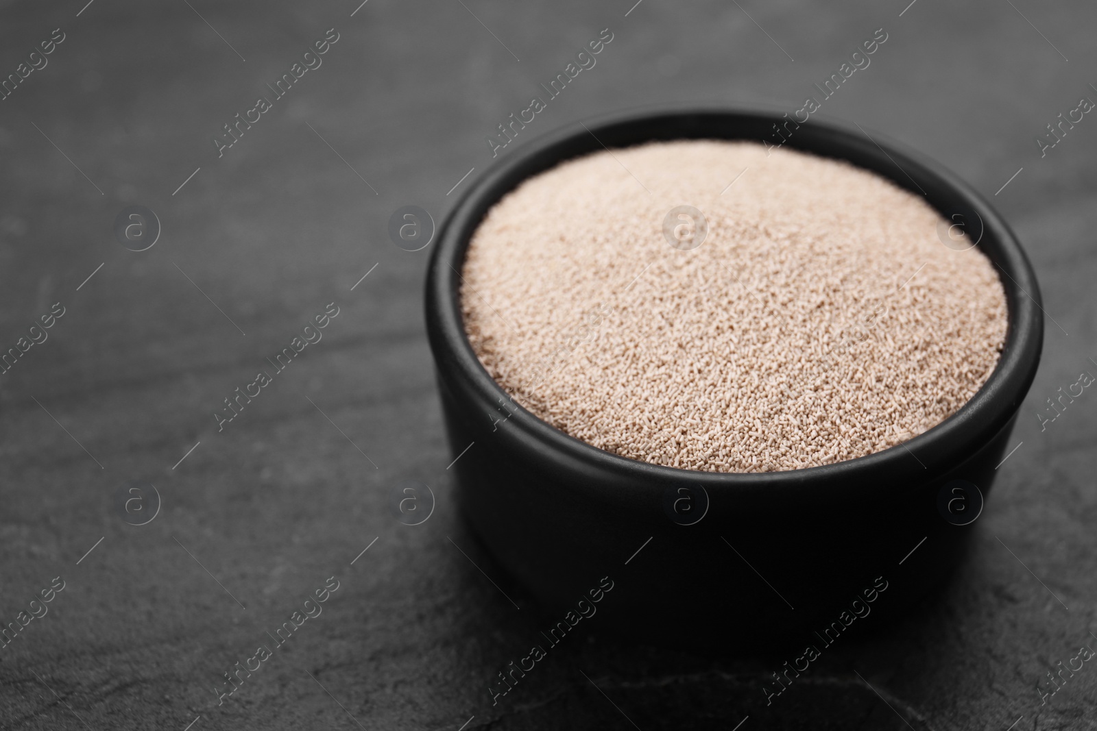 Photo of Bowl of active dry yeast on black table, closeup. Space for text