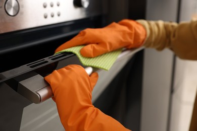 Woman with microfiber cloth cleaning electric oven in kitchen, closeup