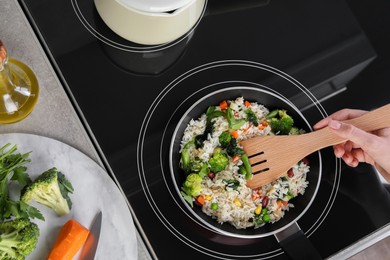 Photo of Woman frying rice with vegetables on induction stove, top view