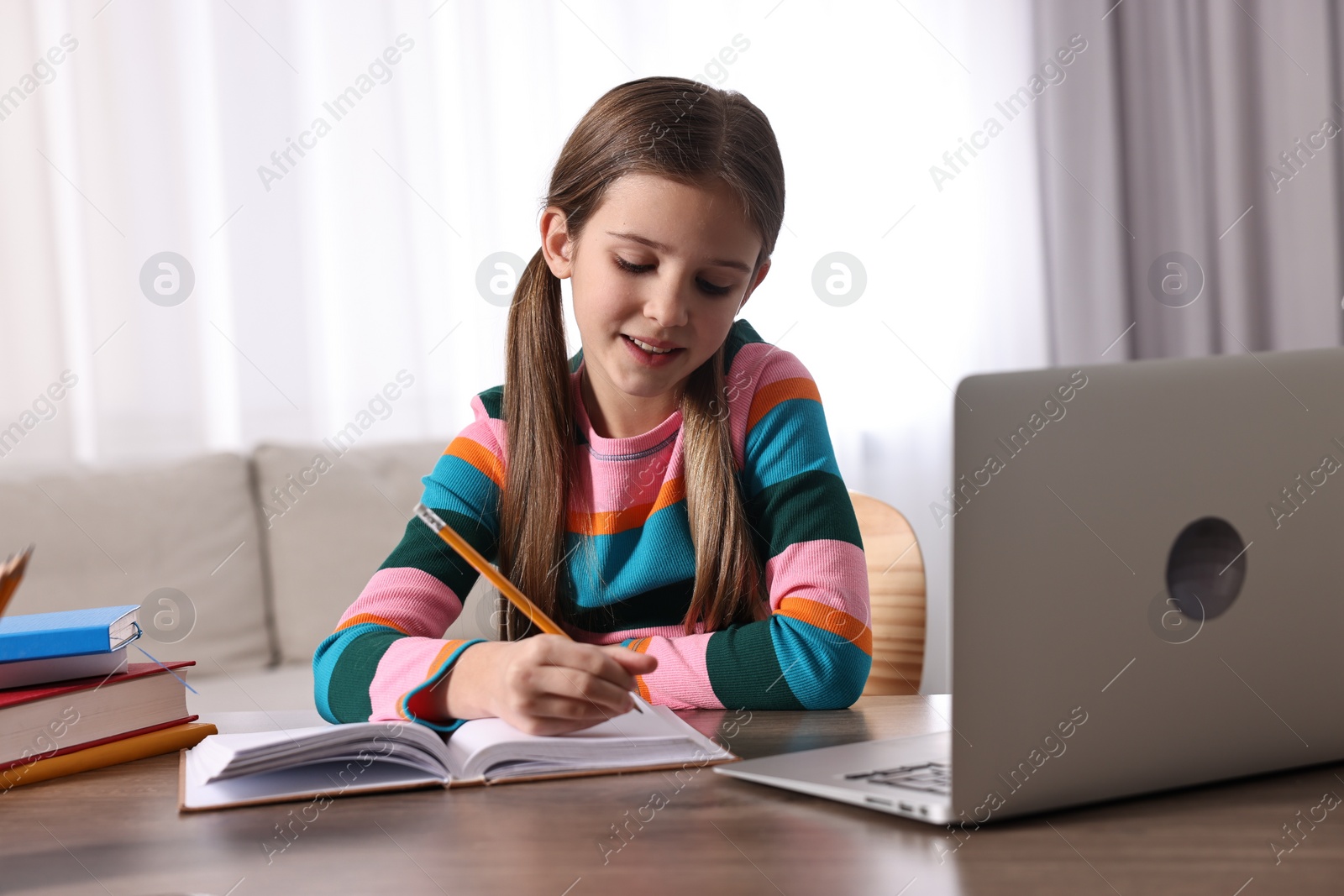 Photo of E-learning. Cute girl taking notes during online lesson at table indoors