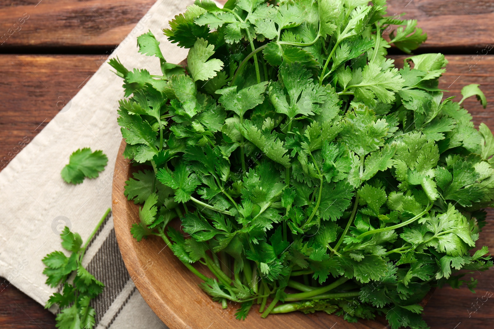 Photo of Fresh coriander in bowl on wooden table, top view