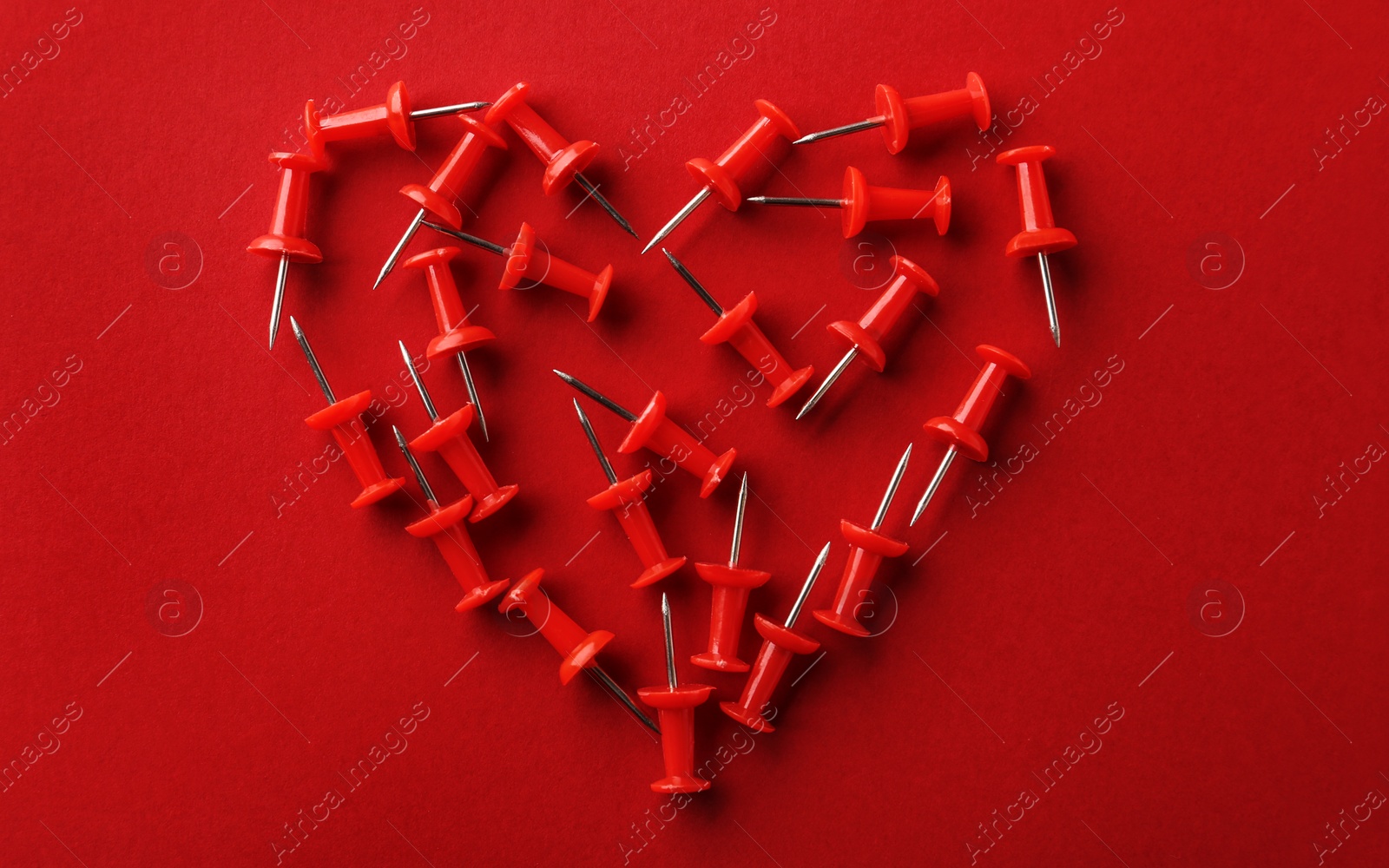 Photo of Heart shaped pile of pins on red background, flat lay