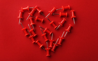 Photo of Heart shaped pile of pins on red background, flat lay