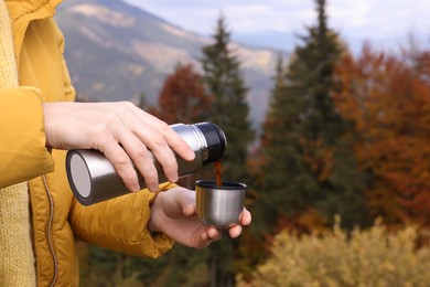 Photo of Young woman pouring instant coffee into mug in mountains, closeup