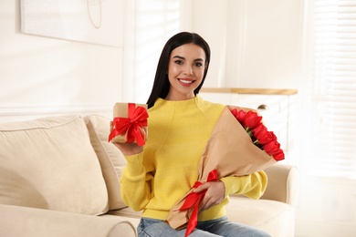 Photo of Happy woman with red tulip bouquet and gift box at home. 8th of March celebration