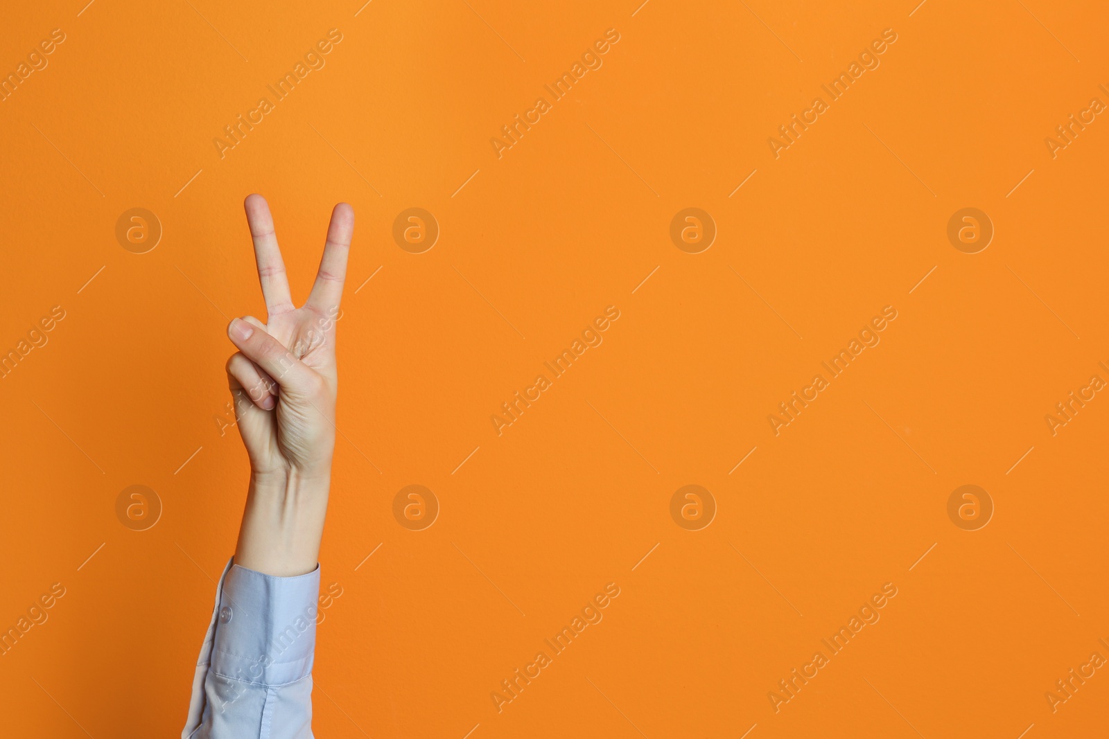 Photo of Young woman showing victory gesture on color background. Space for text