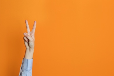 Photo of Young woman showing victory gesture on color background. Space for text