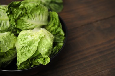 Bowl of fresh green romaine lettuces on wooden table, closeup. Space for text