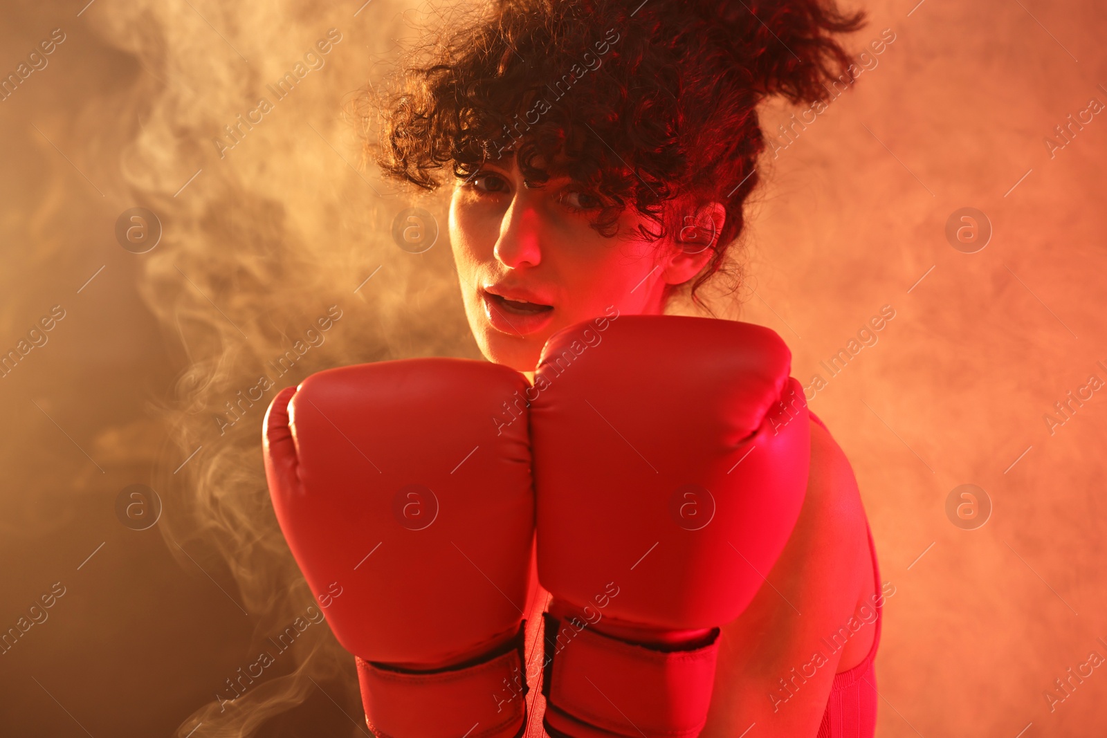 Photo of Beautiful young woman with boxing gloves on color background in neon lights and smoke