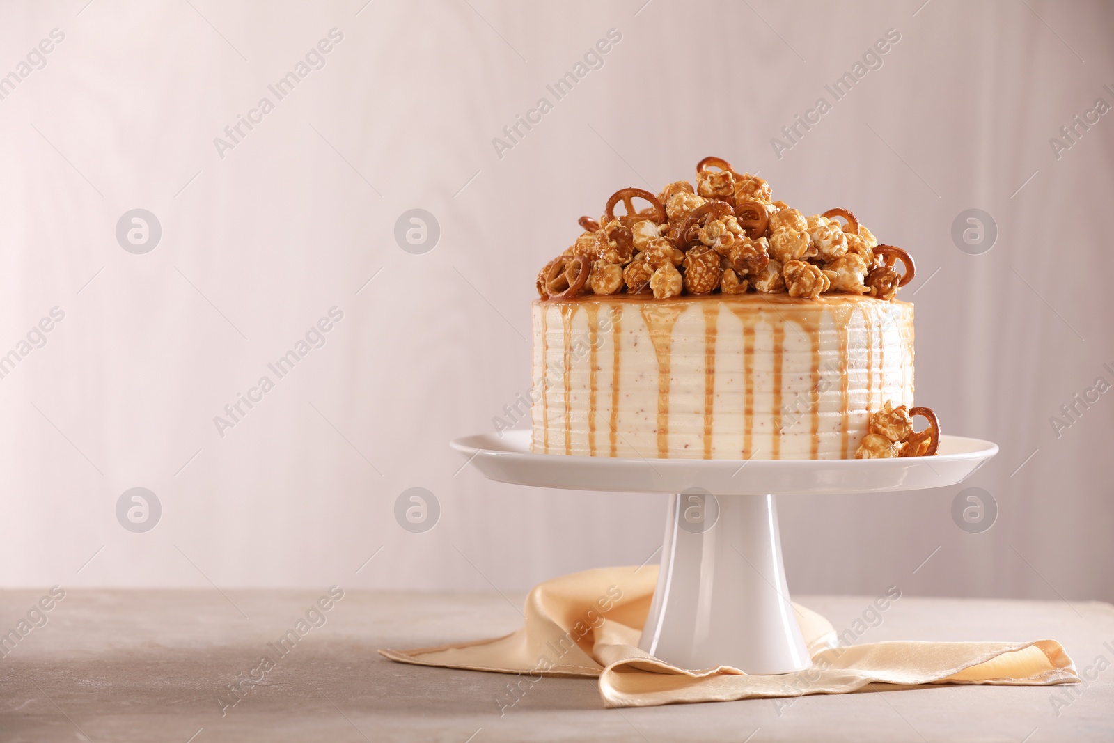 Photo of Caramel drip cake decorated with popcorn and pretzels on light grey table, space for text