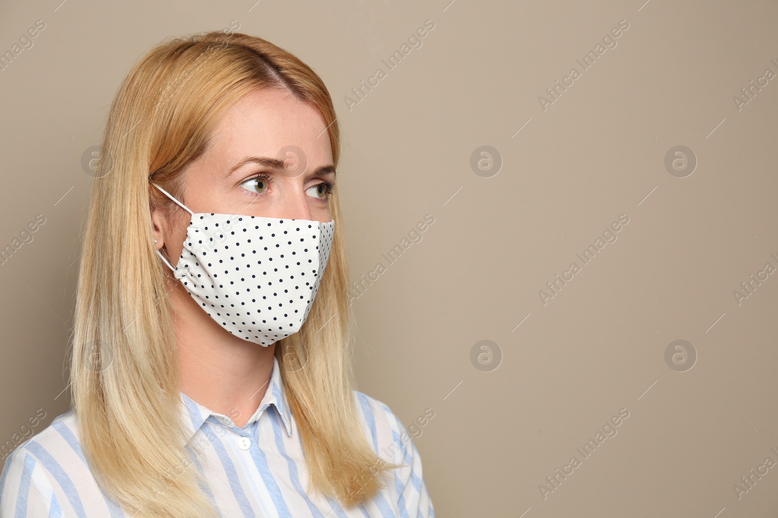 Photo of Woman wearing handmade cloth mask on beige background, space for text. Personal protective equipment during COVID-19 pandemic