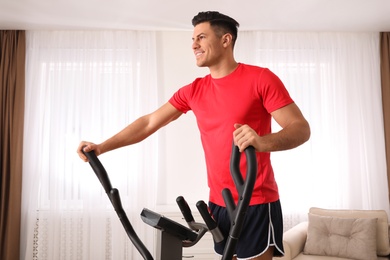 Man using modern elliptical machine at home