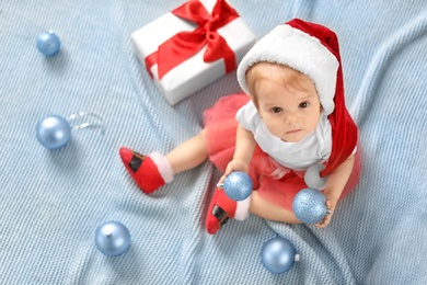 Photo of Cute baby in festive costume playing with Christmas decor on blanket