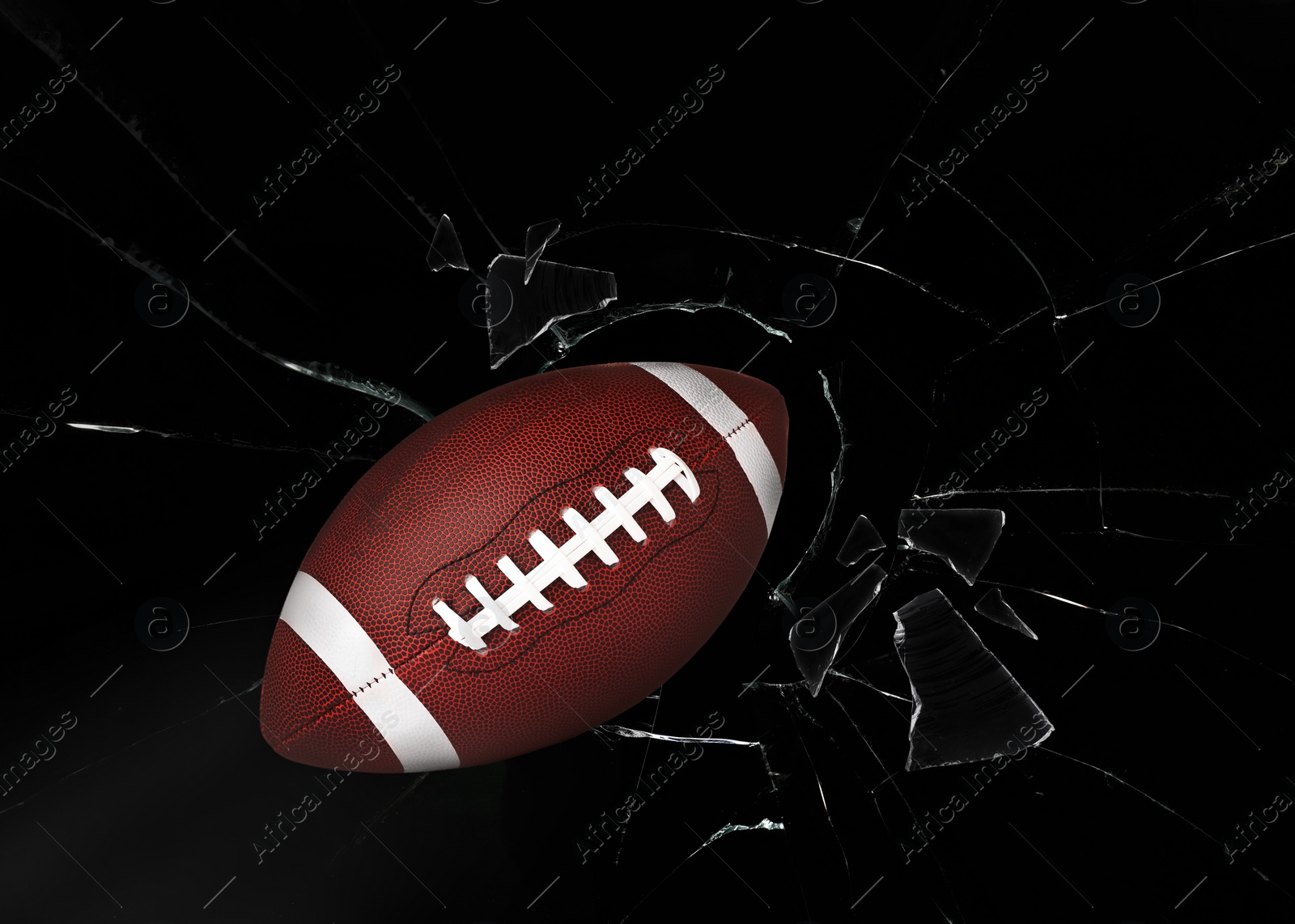 Image of American football ball breaking up glass against black background