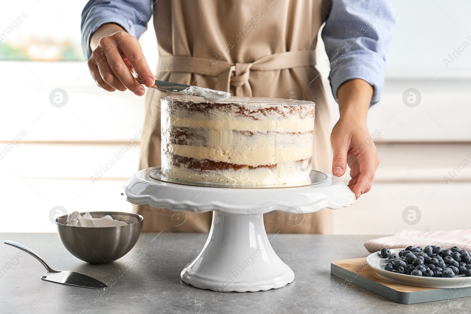 Photo of Woman decorating delicious cake with fresh cream on stand. Homemade pastry