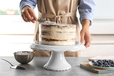 Woman decorating delicious cake with fresh cream on stand. Homemade pastry