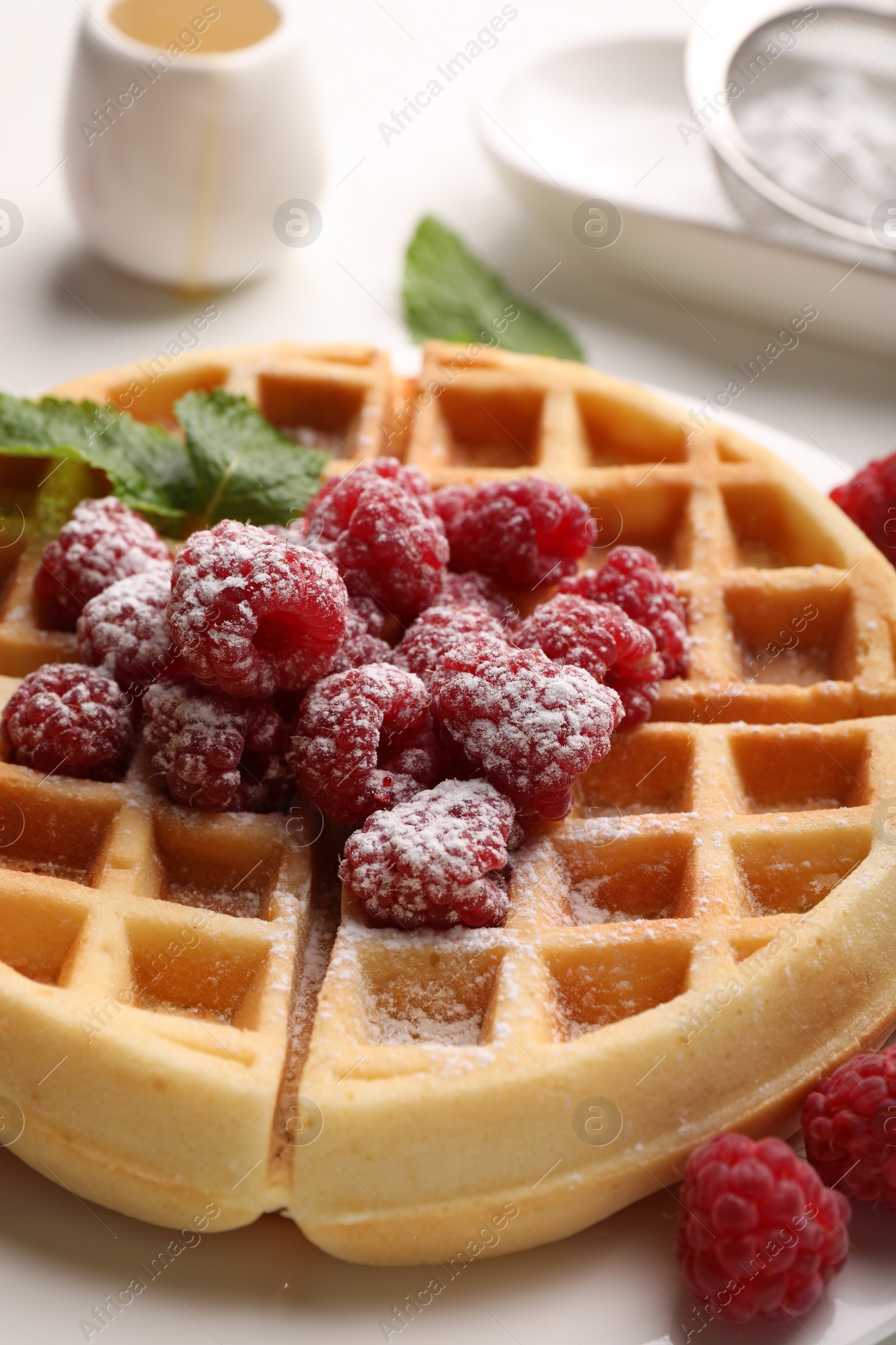 Photo of Tasty Belgian waffle with fresh raspberries, powdered sugar and mint on table, closeup