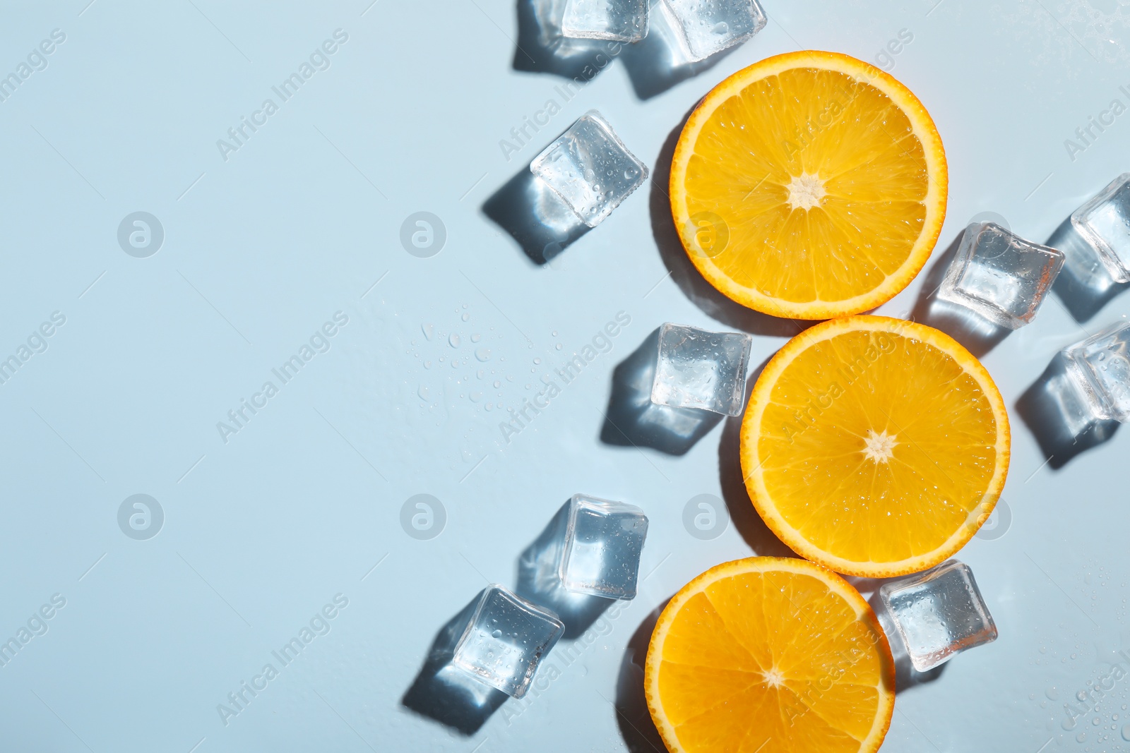 Photo of Slices of juicy orange and ice cubes on light blue background, flat lay. Space for text