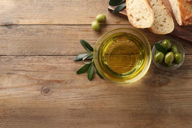 Photo of Glass bowl of oil, ripe olives and bread on wooden table, flat lay. Space for text