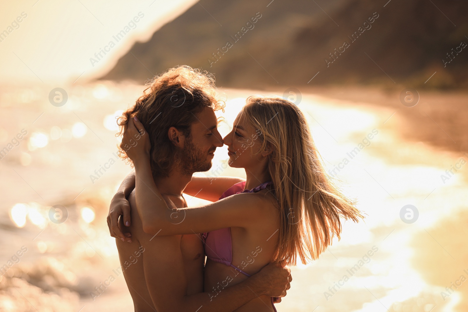 Photo of Young woman in bikini kissing her boyfriend on beach at sunset. Lovely couple