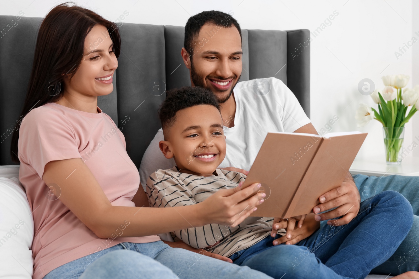 Photo of Happy international family reading book on bed