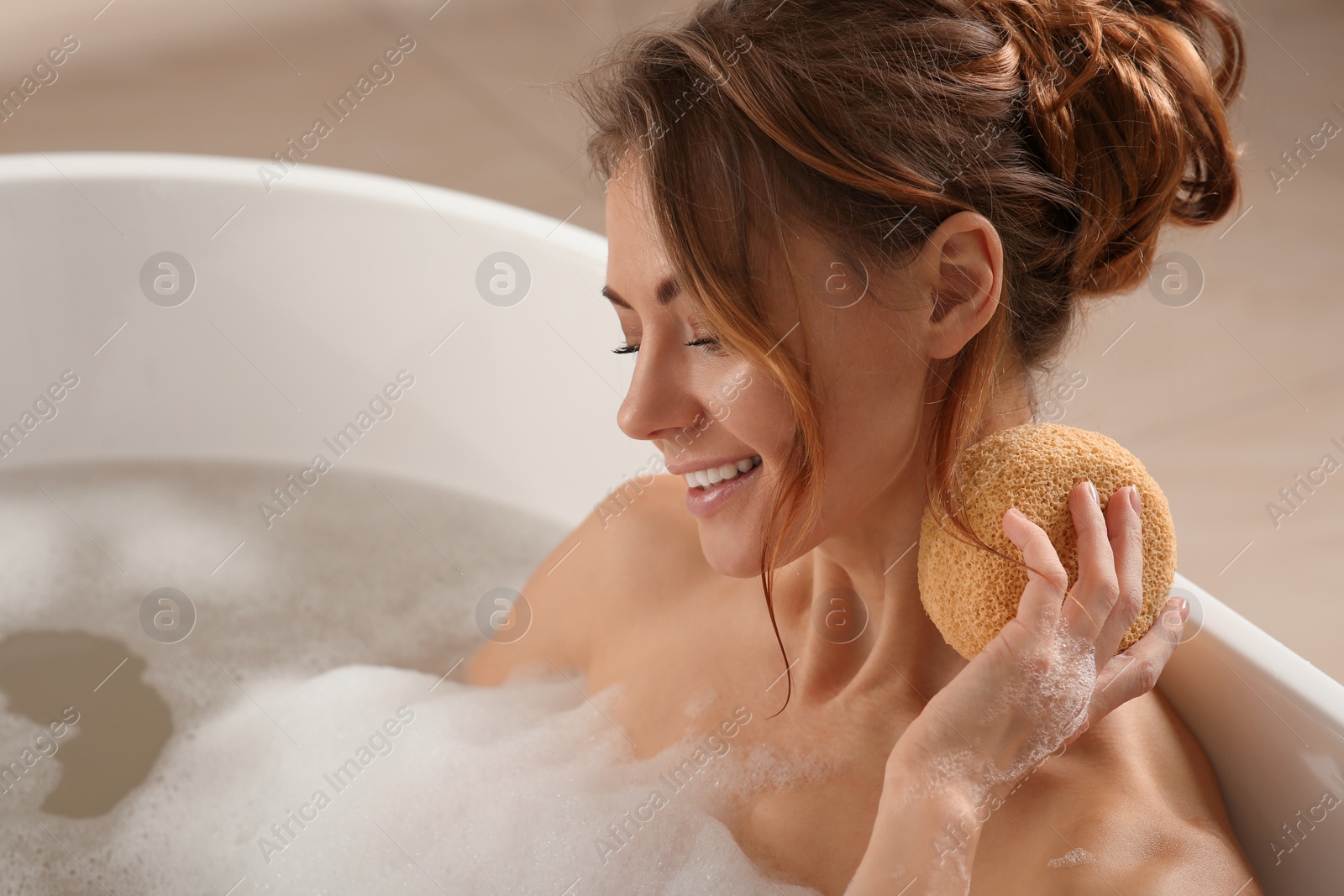 Photo of Beautiful woman rubbing neck with sponge while taking bath