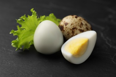 Unpeeled and peeled hard boiled quail eggs with lettuce leaf on black table, closeup