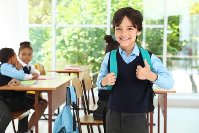 Boy wearing school uniform with backpack in classroom