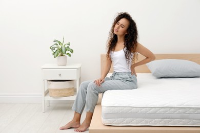 Young African American woman suffering from back pain after sleeping on uncomfortable mattress in bedroom