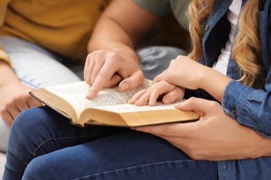 Photo of Girl and her godparents reading Bible together indoors, closeup