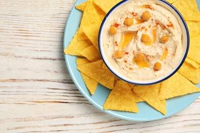 Photo of Bowl of tasty hummus with chickpeas, paprika and crispy chips on white wooden table, top view. Space for text