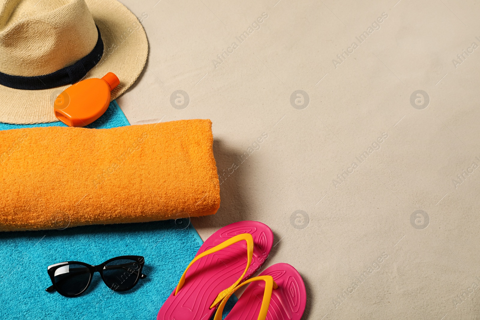 Photo of Beach towels, hat, sunscreen, sunglasses and flip flops on sand. Space for text