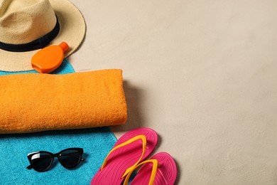 Photo of Beach towels, hat, sunscreen, sunglasses and flip flops on sand. Space for text