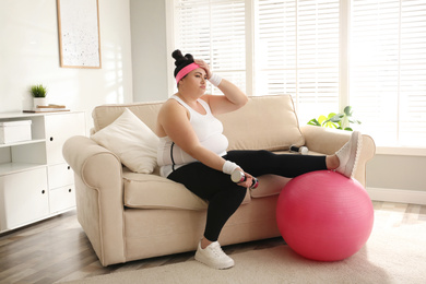 Photo of Lazy overweight woman with sport equipment on sofa at home