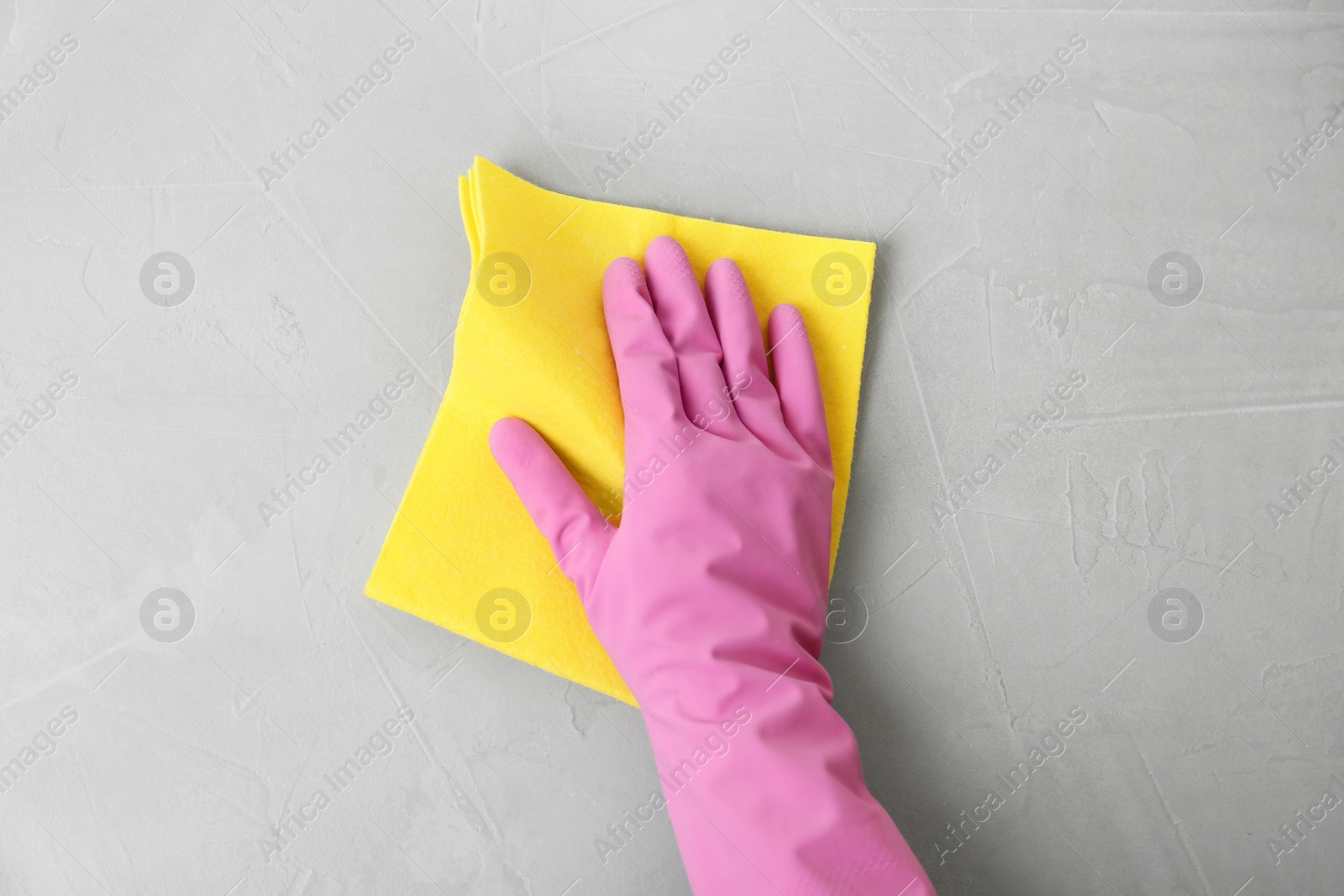 Photo of Woman in gloves wiping grey table with rag, top view