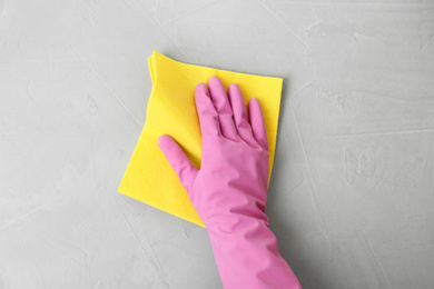 Woman in gloves wiping grey table with rag, top view