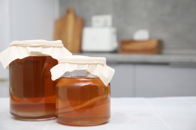 Photo of Homemade fermented kombucha in glass jars on white table in kitchen. Space for text