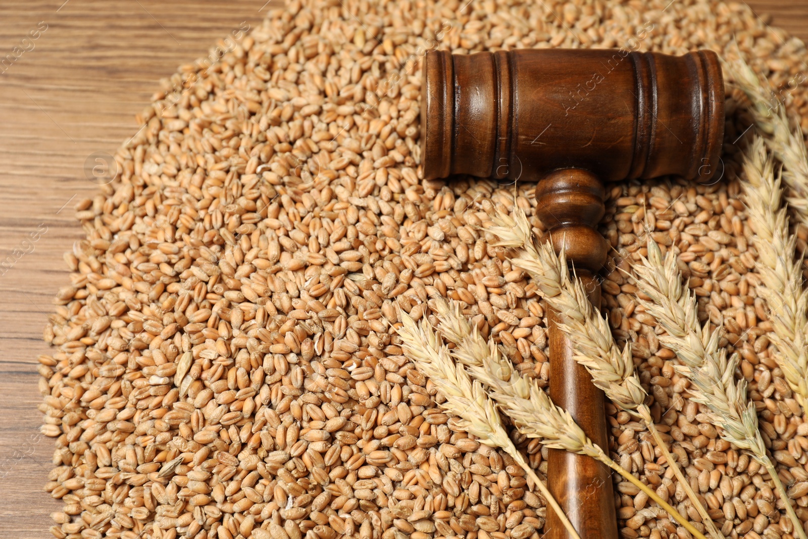 Photo of Judge's gavel, wheat ears and grains on wooden table, closeup. Agricultural deal