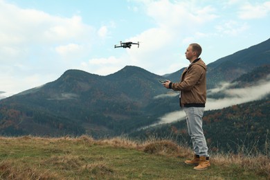 Young man operating modern drone with remote control in mountains, space for text