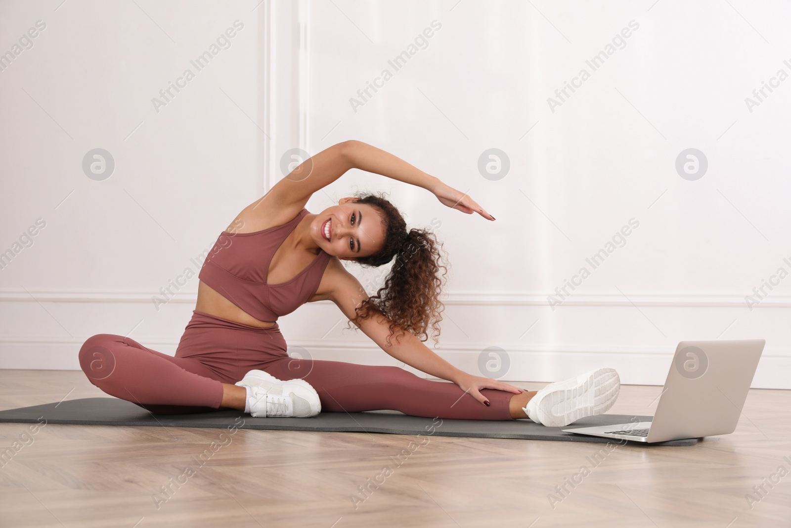 Photo of Beautiful African American woman stretching on yoga mat while watching online class indoors